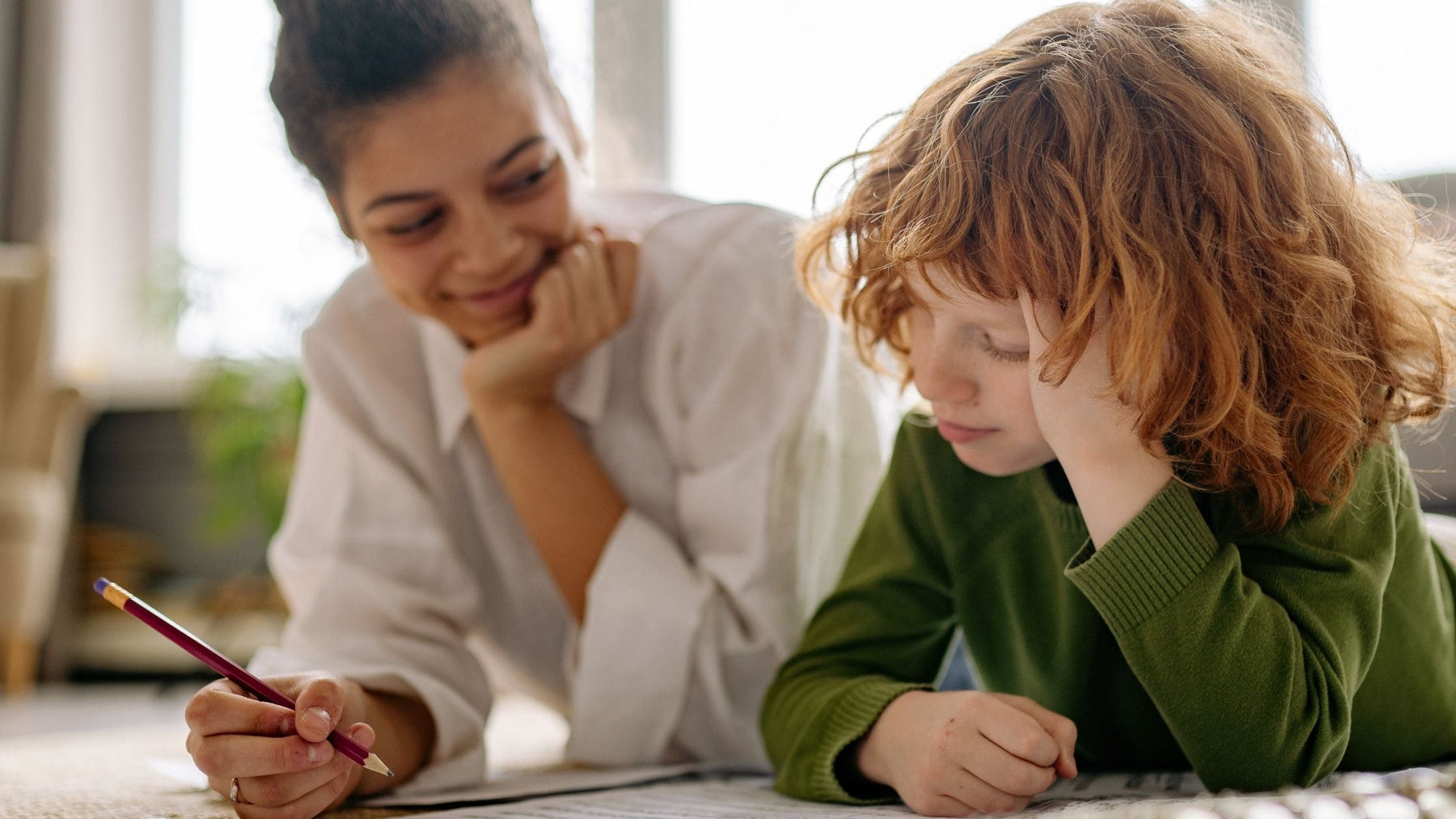 A supportive mother practicing the body doubling ADHD hack while her young son focuses on his schoolwork and writing tasks.