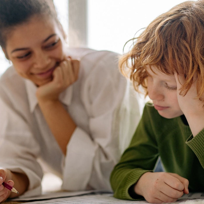 A supportive mother practicing the body doubling ADHD hack while her young son focuses on his schoolwork and writing tasks.