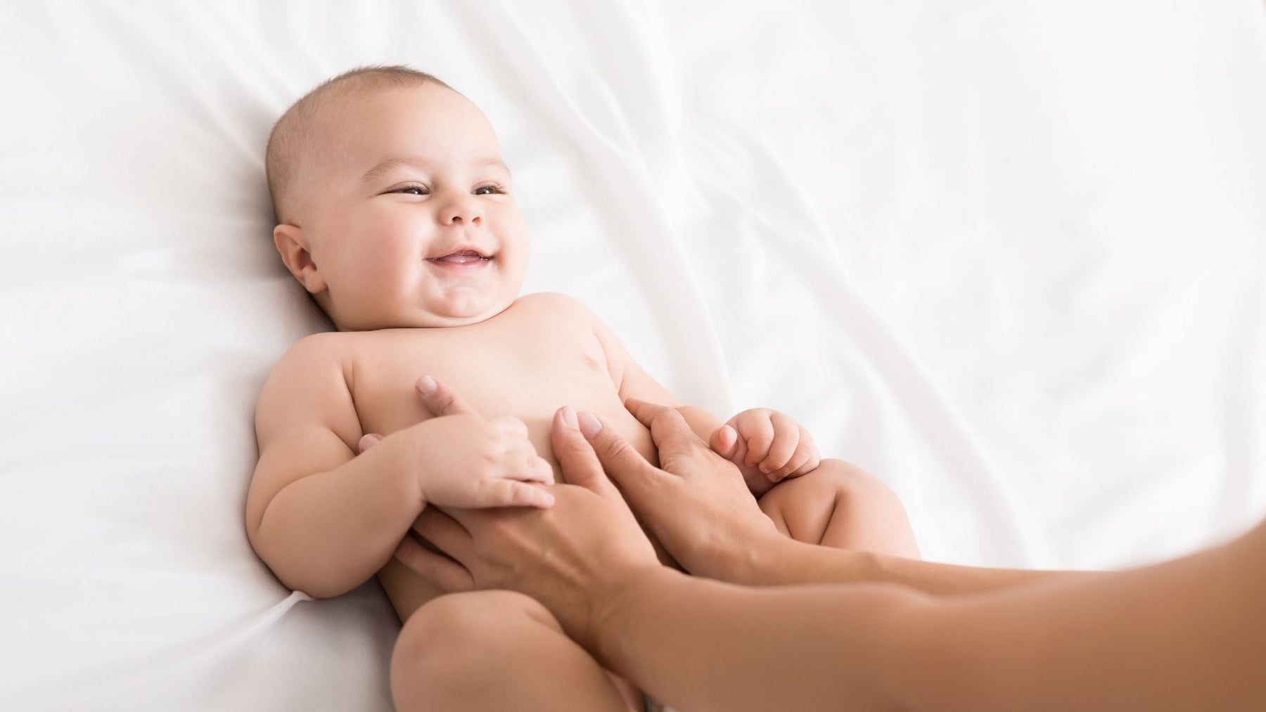 A happy baby smiling during a gentle tummy massage on a white bed.