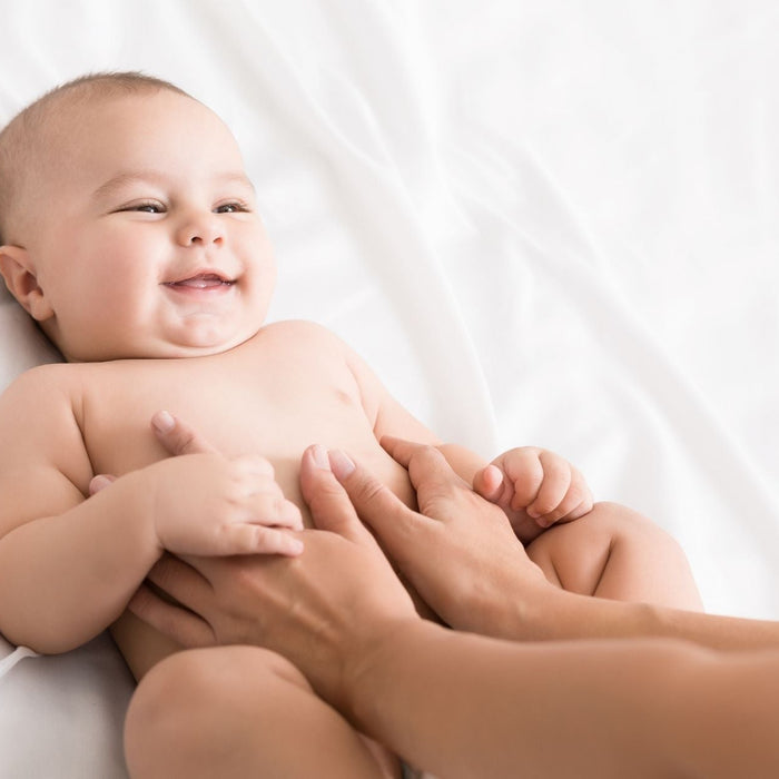 A happy baby smiling during a gentle tummy massage on a white bed.