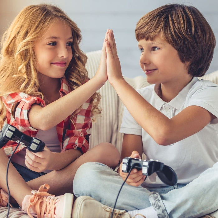 Young girl and boy smiling and high-fiving while playing video games at home, representing how ADHD can show up differently in girls and boys.