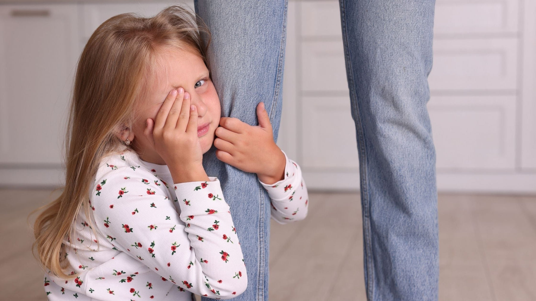 Young child holding onto a parent’s leg, showing separation anxiety and emotional overwhelm during a transition moment