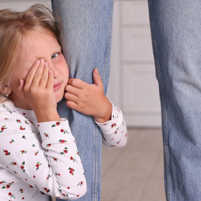 Young child holding onto a parent’s leg, showing separation anxiety and emotional overwhelm during a transition moment