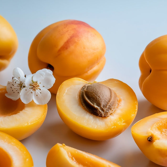 Fresh ripe orange apricots sliced open to reveal the inner pit and kernel, arranged on a clean white background with small white blossoms.