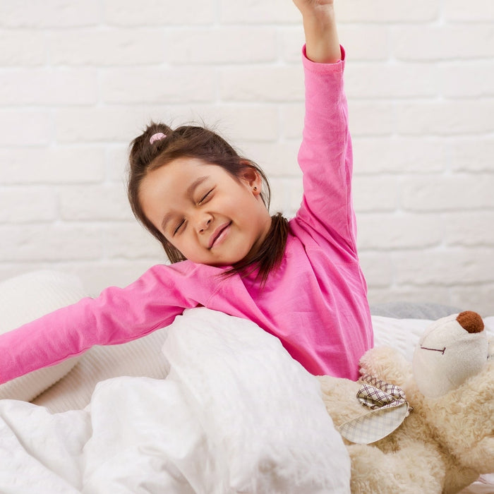 A young girl stretching and waking up refreshed in bed to start a focused school morning routine.