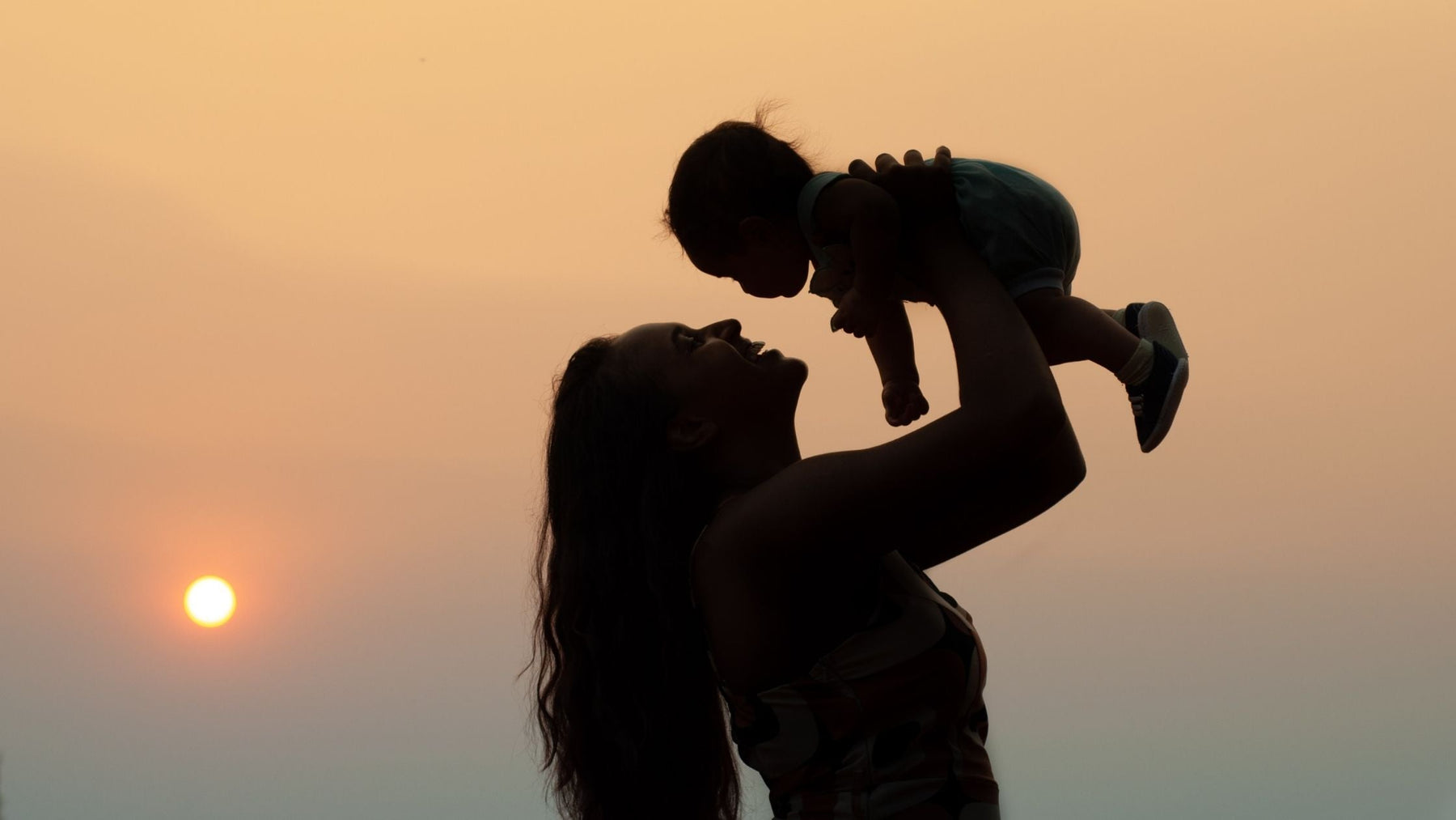 Mother holding baby at sunset, symbolizing ADHD's genetic connection between parent and child.