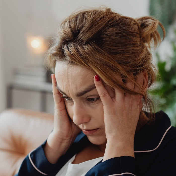 Woman holding her head, looking exhausted and distracted, suffering from brain fog