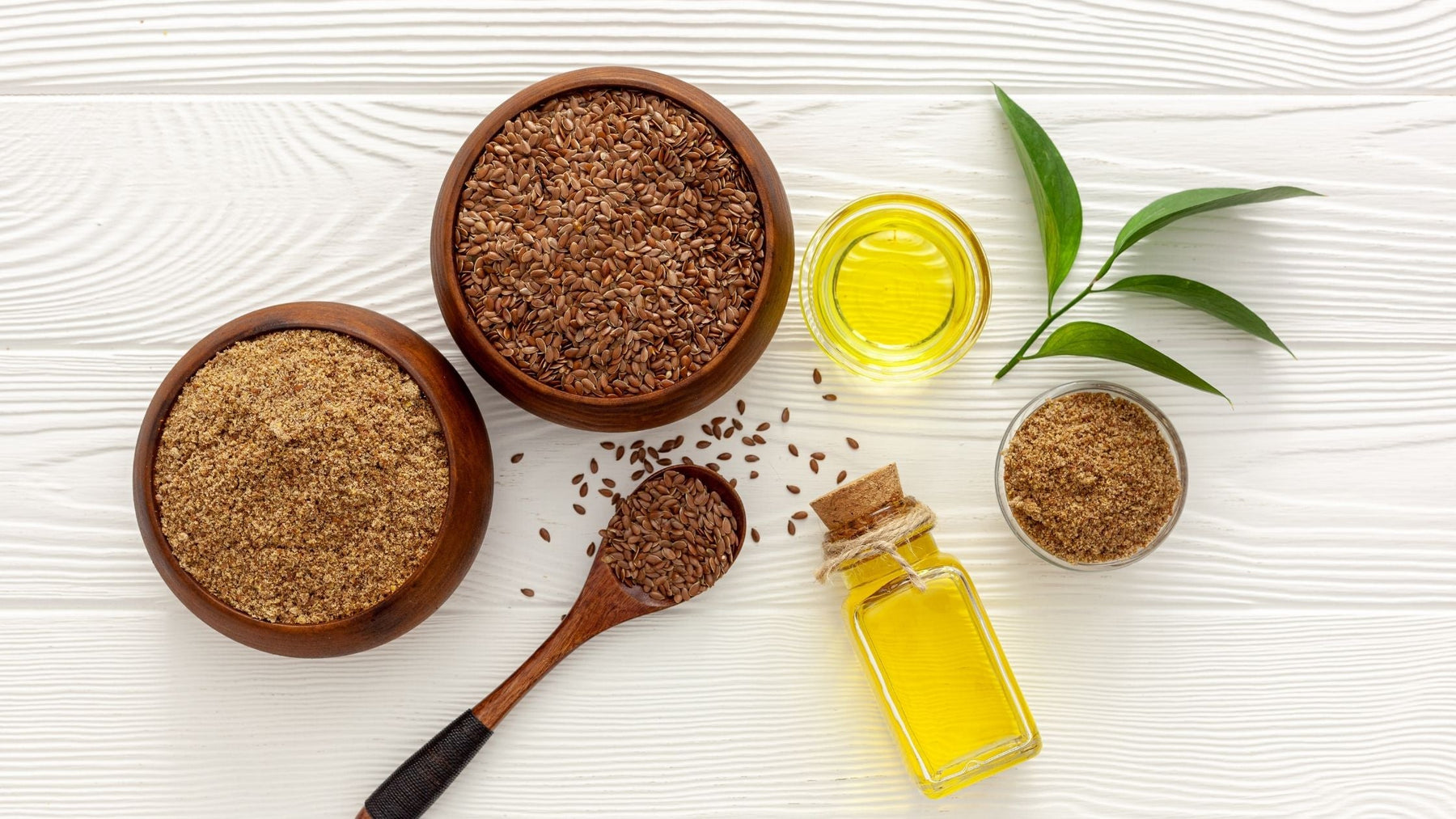 Flax seeds, ground flax, and flaxseed oil in bowls and bottles on a white surface