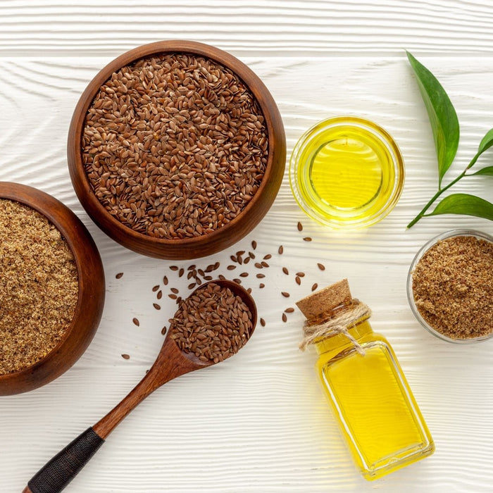 Flax seeds, ground flax, and flaxseed oil in bowls and bottles on a white surface