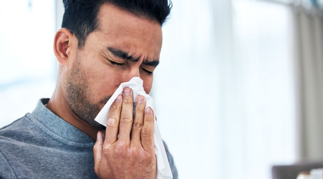 Man sneezing into a tissue, showing common symptoms of sinus infection vs allergies such as congestion, runny nose, and sinus pressure.