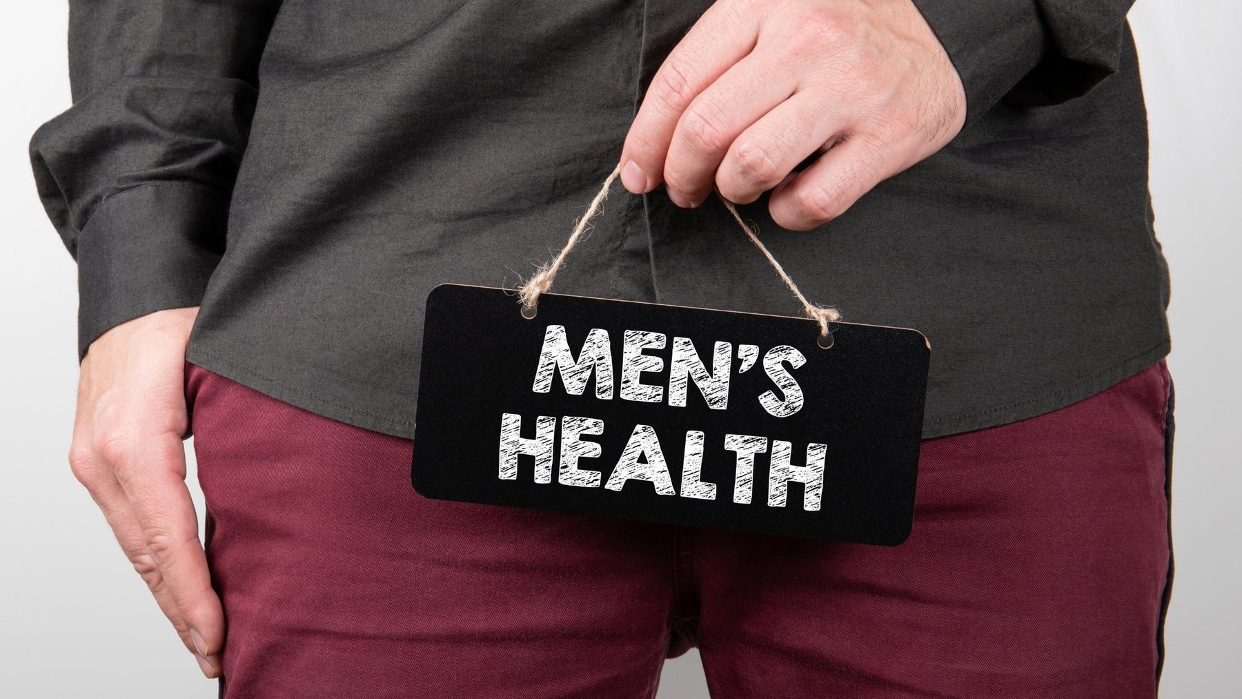 A man holding a small black chalkboard sign that reads "MEN'S HEALTH" in front of his torso, representing male reproductive vitality and fertility care.