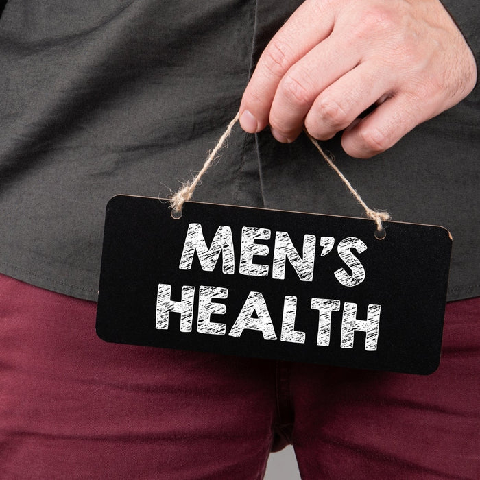 A man holding a small black chalkboard sign that reads "MEN'S HEALTH" in front of his torso, representing male reproductive vitality and fertility care.