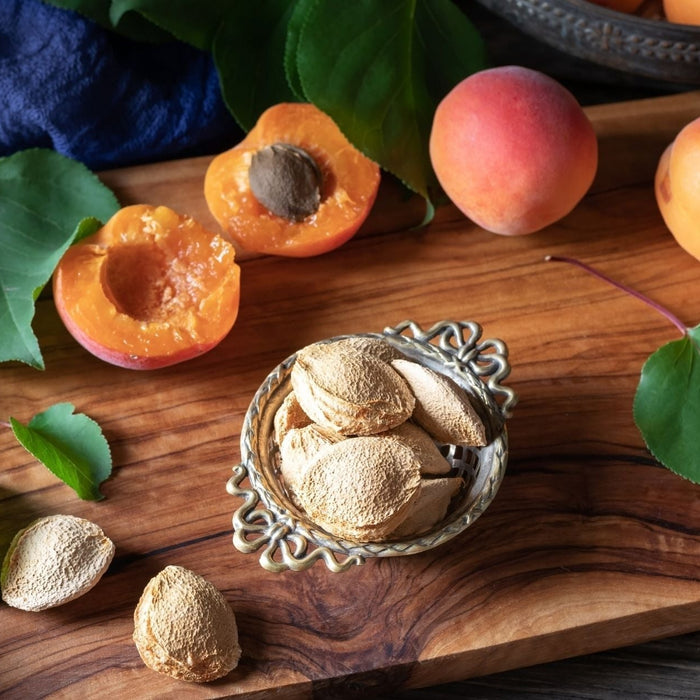 Bitter apricot kernels displayed with fresh apricots and leaves on a wooden board - natural source of vitamin B17 and amygdalin used in holistic wellness.