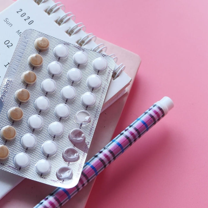 Pack of birth control pills sitting on a calendar planner with a pen on a pink background.