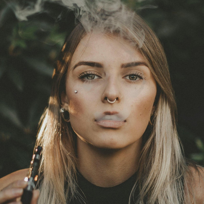 Young woman exhaling vape smoke outdoors while holding a vape device, illustrating stress-induced vaping cravings.