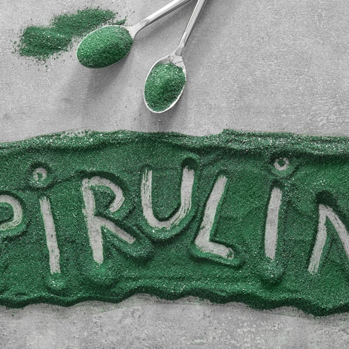 Green spirulina powder arranged on a grey surface with the word ‘spirulina’ written through the powder